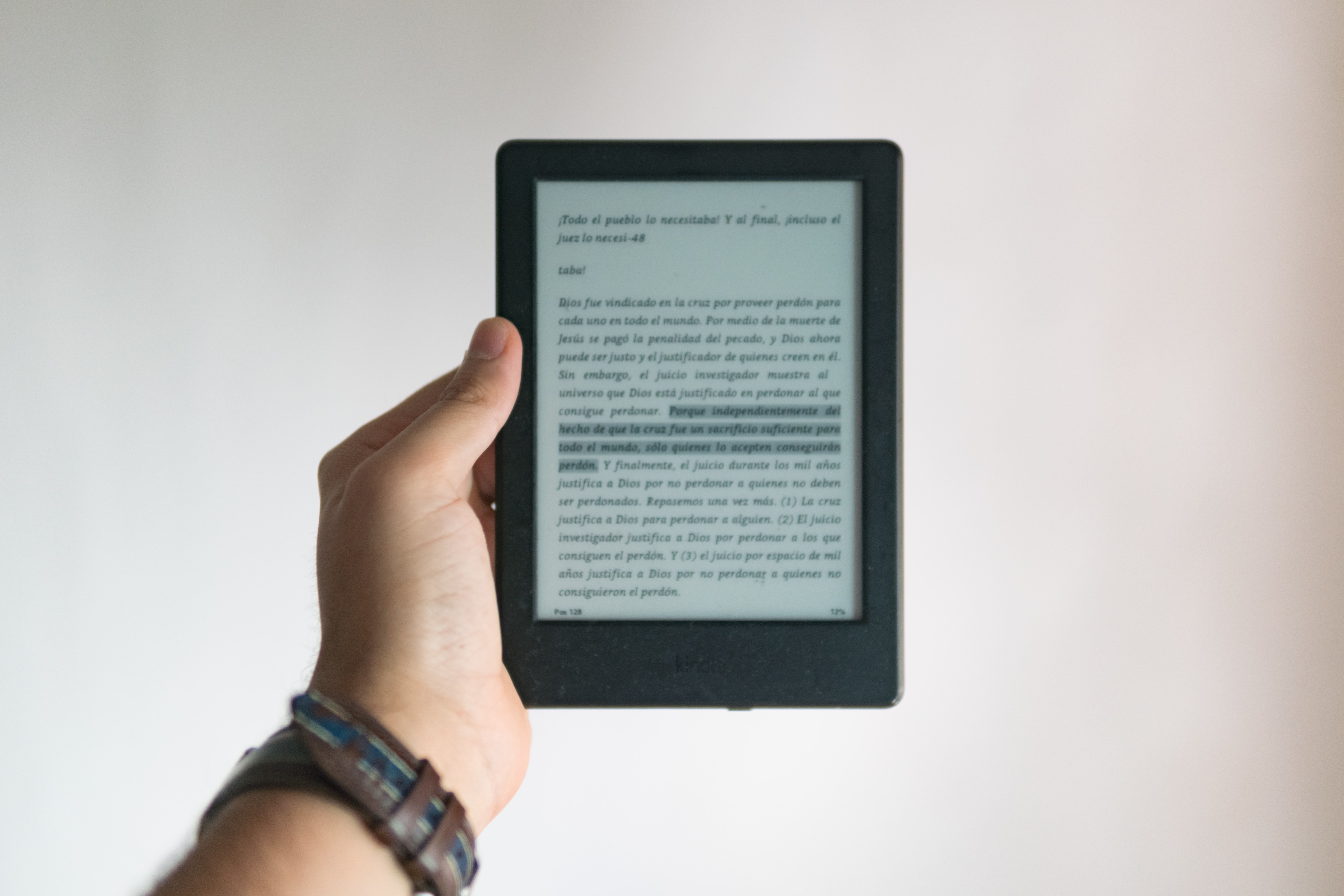 A hand is holding a kindle showing text against a white wall 